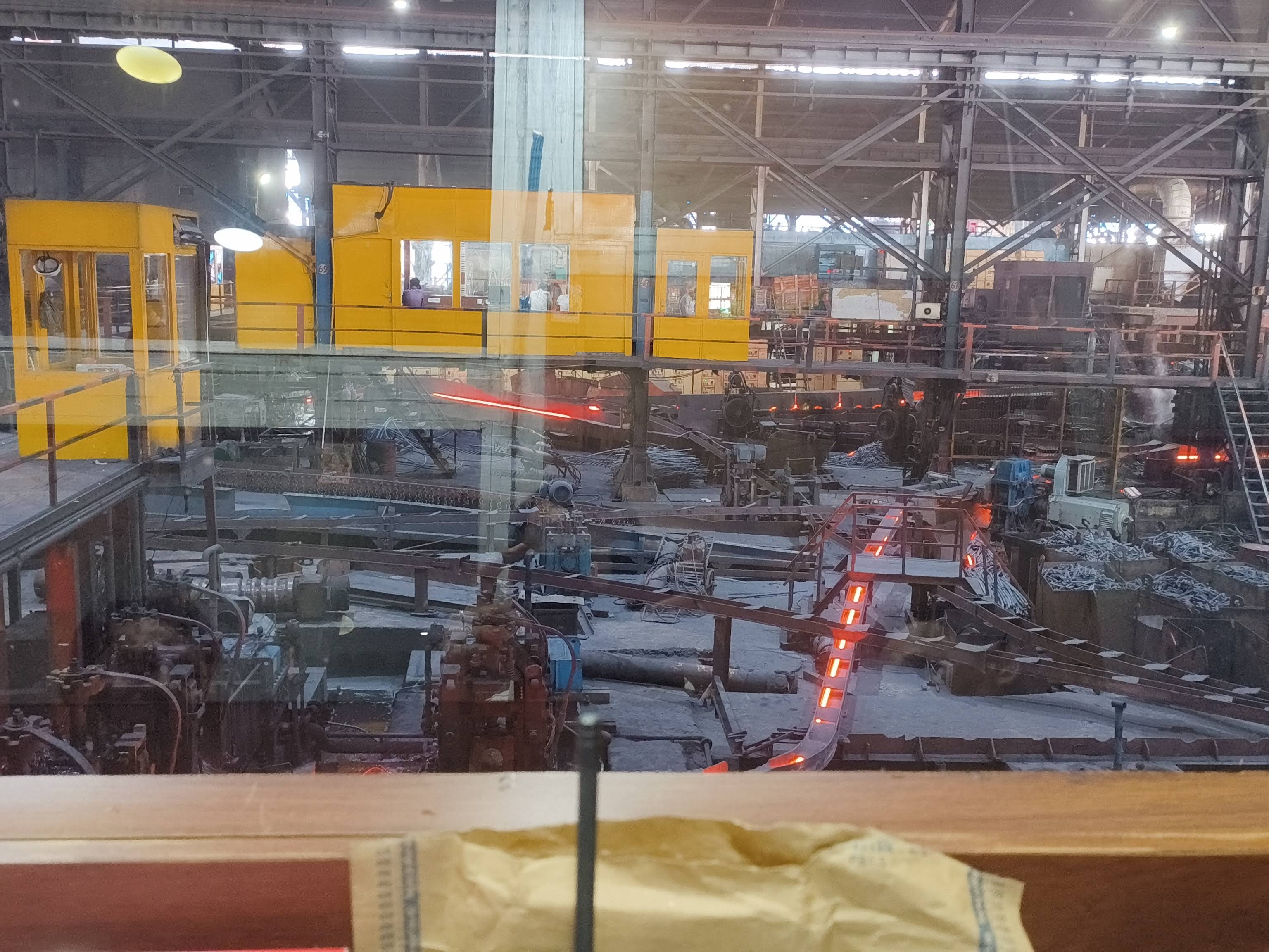 View through glass — yellow control cabins and glowing steel